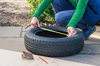 Woman using measuring tape to measure width of car tyre
