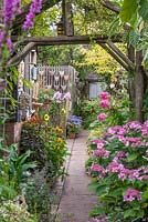 Rustic arch frames a view along a path, leading past pink hydrangeas and phlox. On left, hot coloured dahlias and rudbeckias.
