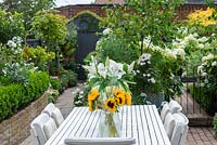 Dining table with vases of sunflowers and white lilies of sunflowers and white lilies against backdrop of white agapanthus, fuchsia,  hydrangeas, geraniums, cosmos, roses, gaura, busy lizzies and silver birches.