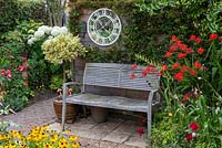 Bench sits beneath a clock mirror, flanked by crocosmia on the right, and on the left, a variegated euonymus standard in a pot.