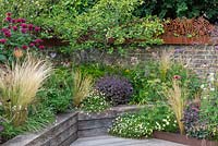 Raised, wooden beds planted with ornamental grasses, Erigeron and small Amelanchier, backed by brick wall topped by corton steel panels.