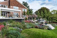 An award-winning house design from the 1970s, with contemporary outdoor decks and terraces wrapped in autumn borders of herbaceous flowering plants and ornamental grasses.