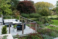 The middle deck edged in autumn borders of pennisetum, miscanthus, catmint, salvias, Verbena bonariensis, globe thistles, persicaria, hardy geraniums and sedums. Set against backdrop of mature trees and countryside.