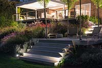 Contemporary decks and steps lit at night, illuminating surrounding borders of ornamental grasses and flowering perennials.