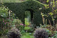 An arch is cut into an old yew hedge, framing a view of the vegetable patch beyond. 