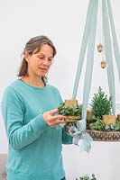 Woman placing candle holder with foliage onto hanging tray