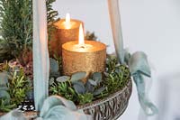 Detail of hanging advent arrangement with gold candles, miniature Christmas tree and Eucalyptus and Hebe foliage. 
