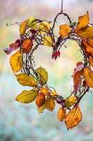 Simple heart shaped willow wreath with autumnal Hornbeam foliage and fairy lights, hanging in shed window with view to garden. 