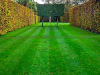 Carpinus betulus - Hornbeam - hedges enclose neat lawn with trained tree arch framing sculpture