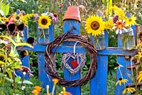 Floral glass jar with sunflowers, dahlias, zinnias, coneflowers and other late summer flowers hanging on a blue painted wooden fence.