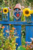 Floral glass jar with sunflowers hanging on a blue painted wooden gate.
