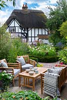View from sitting area towards yew-edged beds of tall perennials, ornamental grasses and Cosmos, thatched cottage beyond 