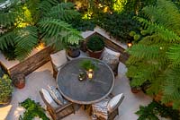 A bird's-eye view of an enclosed courtyard with outdoor dining, fronds of Dicksonia antarctica - Tree Fern - filtering the light from uplighters