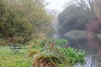 River view on a misty autumn morning. A vintage wood and metal garden seat  overlooks the tree lined River Wylye