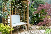 Trellis arbour with climber set in gravel against a fence 