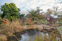 View over garden pond garden with greenhouse beyond