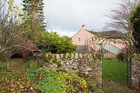 View of house with lean-to greenhouse from stone wall with metal arch