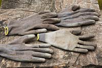 Worn grey cotton and rubber gardening work gloves on wooden surface