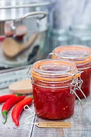 Chilli jam in kilner jar, chillies and tools for jam making with German label. 