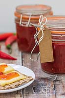 Chilli jam in kilner jar, chillies and plate of crackers and cheese.