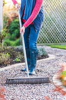 Woman using a wdie brush to level a gravel path
