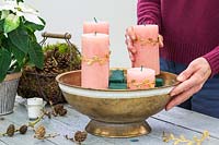 Woman adding pillar candles to bowl in between floral foam blocks