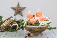 Floral arrangement in a golden bowl, with four pillar candles, Poinsettia flowers, cones and moss