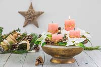 A bowl arrangement in a golden bowl, with four pillar candles, Poinsettia flowers, cones and moss