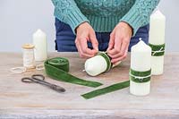 Woman adding a decorative velter green ribbon and cream string to the pillar candle