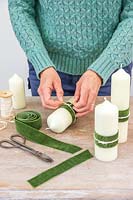 Woman adding a decorative velvet green ribbon and cream string to the pillar candle