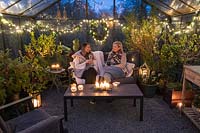 People sat in lounge furniture inside greenhouse decorated for Christmas with fairylights and candles