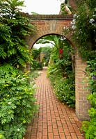 A view through a brick arch along a brick path surrounded by herbaceous borders at East Ruston Old Vicarage