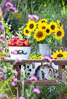 Colander of freshly picked tomatoes and sunflower bouquet in a bucket.