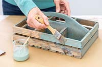 Woman using a brush to paint the wooden box with handle a fresh coat of paint