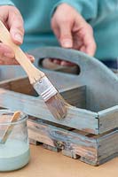 Woman using a brush to paint the wooden box with handle a fresh coat of paint. 