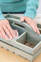 Woman sanding the newly painted wooden box to give a distressed vintage look