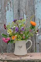 Little jug with flowers in July with Verbena bonariensis, Papaver Poppy seed heads, Calendula officinalis 'Indian Prince', Rosa roses, Alchemilla mollis, 'Erigeron karvinskianus', Annual grasses, Eschscholzia californica. Hogben pottery