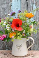 Little jug with flowers in July with Papaver rhoeas - Red poppy, Verbena bonariensis, Papaver Poppy seed heads, Calendula officinalis 'Indian Prince', Rosa roses, Alchemilla mollis, 'Erigeron karvinskianus', Annual grasses, Eschscholzia californica. Hogben pottery