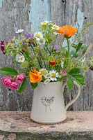 Little jug with flowers in July with Fragaria vesca - alpine strawberry, Tanacetum parthenium - Feverfew, Papaver Poppy seed heads, Calendula officinalis 'Indian Prince', Rosa roses, Alchemilla mollis, 'Erigeron karvinskianus', Annual grasses, Eschscholzia californica. 