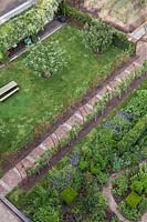 Aerial view of garden with flowerbeds and fruit trees trained on archway linked by brick and stone pathways - Holland, June