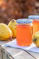 Quince Jelly in jars on table top, with quince fruits, blue gingham lids and table cloth. 