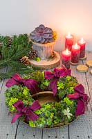Succulent wreath on gold plate with Sempervivum Bronco, Crassula, red pillar candles and red ribbons on rustic table top 