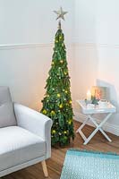Space saving Christmas Tree made with pine - Abies and conifer - Juniperus foliage attached to a willow obelisk and decorated with star decorations and lights in a modern living room setting with chair and sidetable