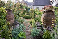Overview of cottage garden with topiary, large urns and informal borders.
