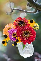 Autumn flower bouquet in glass jar hanging from tree branch.
