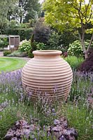View across garden with large decorative terracotta pot surrounded by Heuchera 'Silver Scrolls', Lavandula angustifolia to lawn with flowerbeds containing Acers, Hydrangeas and Catalpa bignonioides 'Aurea' - July, Cheshire