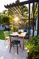 View across dining area with colourful chairs and industrial style pergola at sunset.