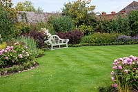 Pink and white themed borders surrounding lawn with Lutyens bench in walled garden. 