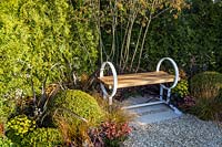 Wooden garden bench next to Buxus sempervirens - Box - balls, Euphorbia, Carex testacea, Phormium 'Platt's Black'. Time is a Healer Garden 