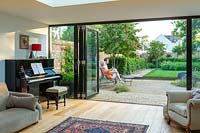 A lounge with bi-fold doors looking on to a contemporary city garden with couple relaxing on a wooden bench.